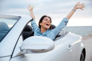 Woman in her convertible car with hands in the air celebrating, because we helped her with a last minute car shipping situation.