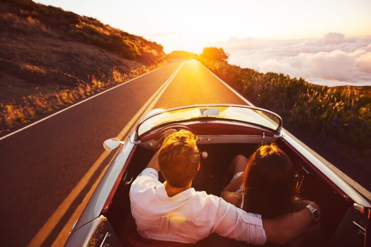 A couple drives in an exotic car at sunset.