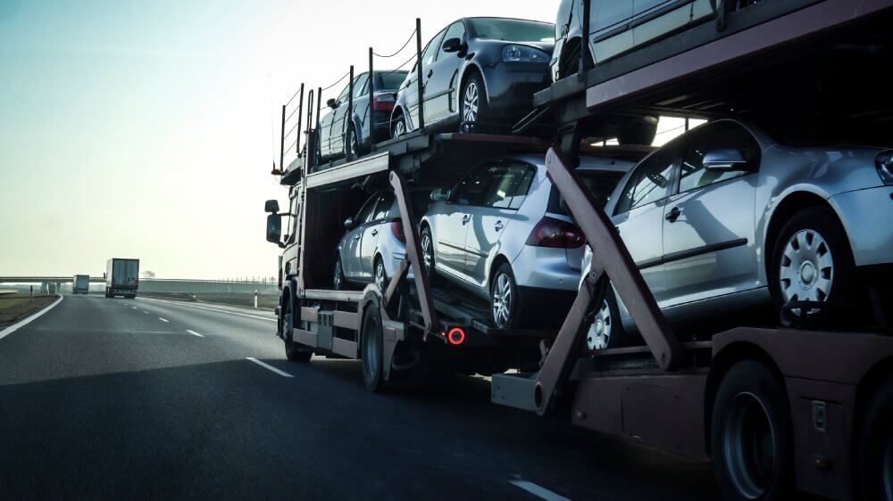 An open car carrier with many vehicles drives on the road. Ship a car across country.