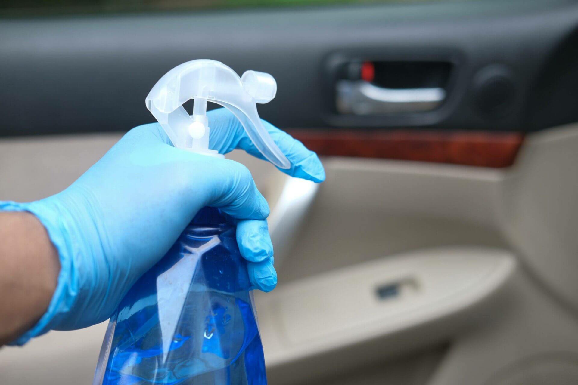 Hand with a blue rubber glove holding a car interior cleaning spray bottle.