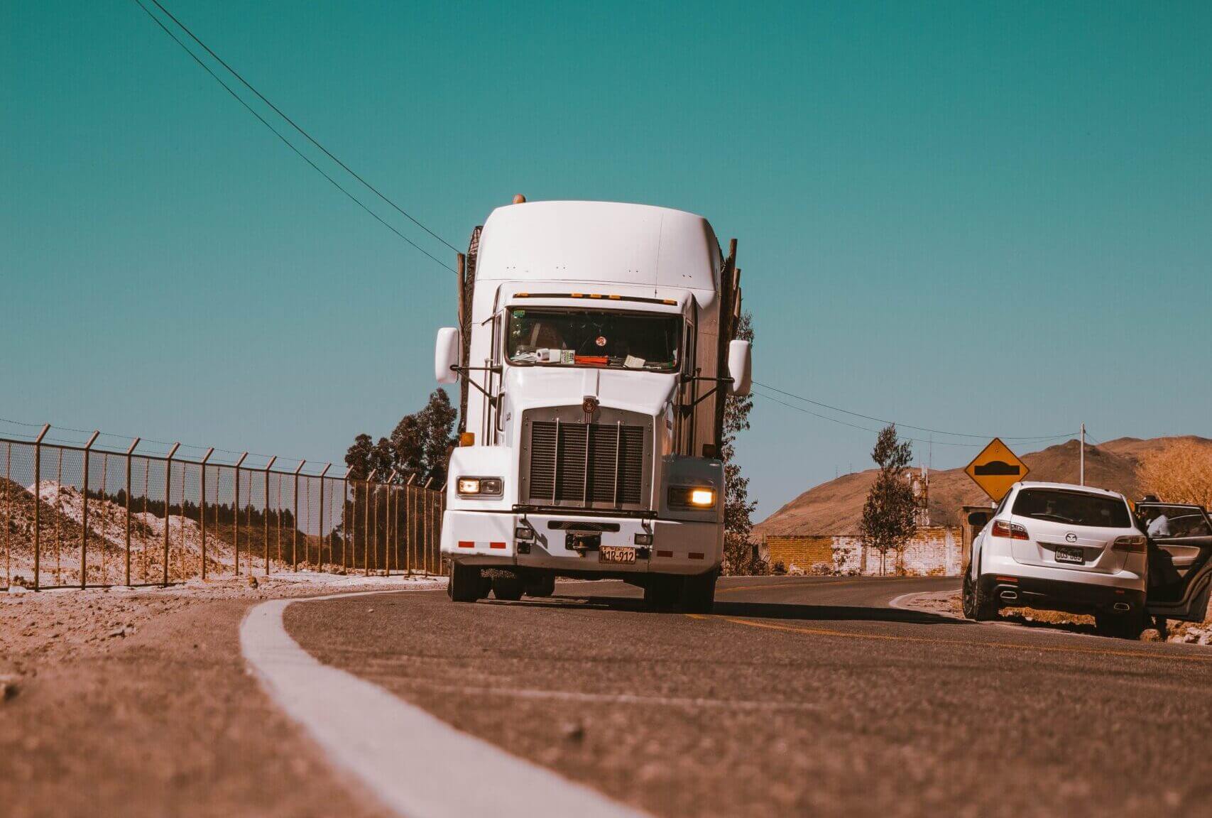 The front of a white semi-truck driving on a highway. Here is a list of the top rated auto transport companies.