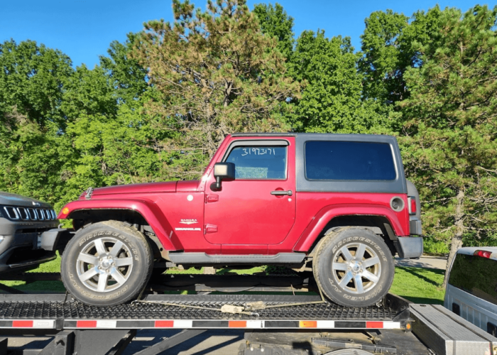 A two-door Jeep Wrangler on an open 3-car wedge trailer.