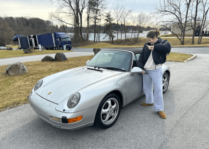 A happy customer with her late 90s Porsche Convertible delivered by an enclosed door-to-door transport trailer in the background to her door.